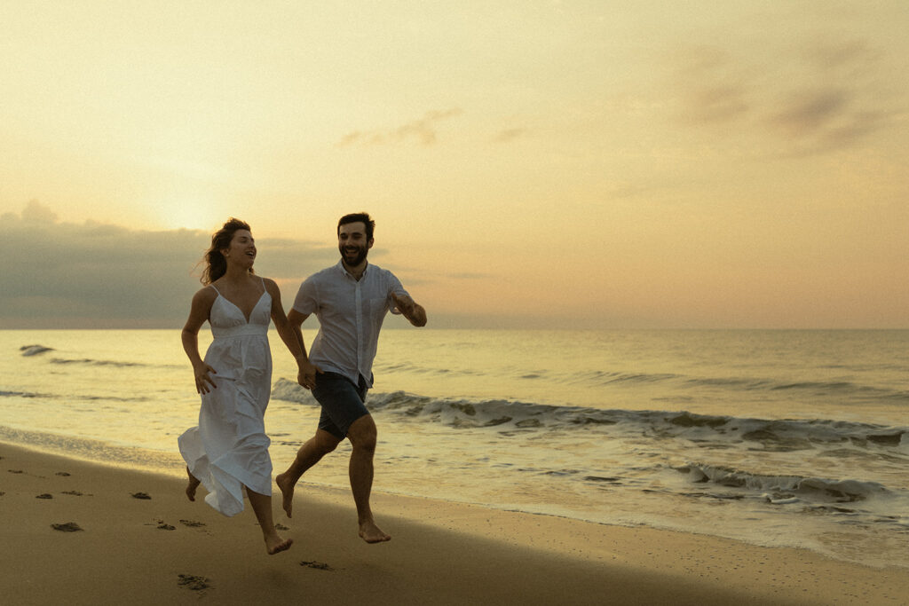 Engaged couple running on the beach together at sunrise